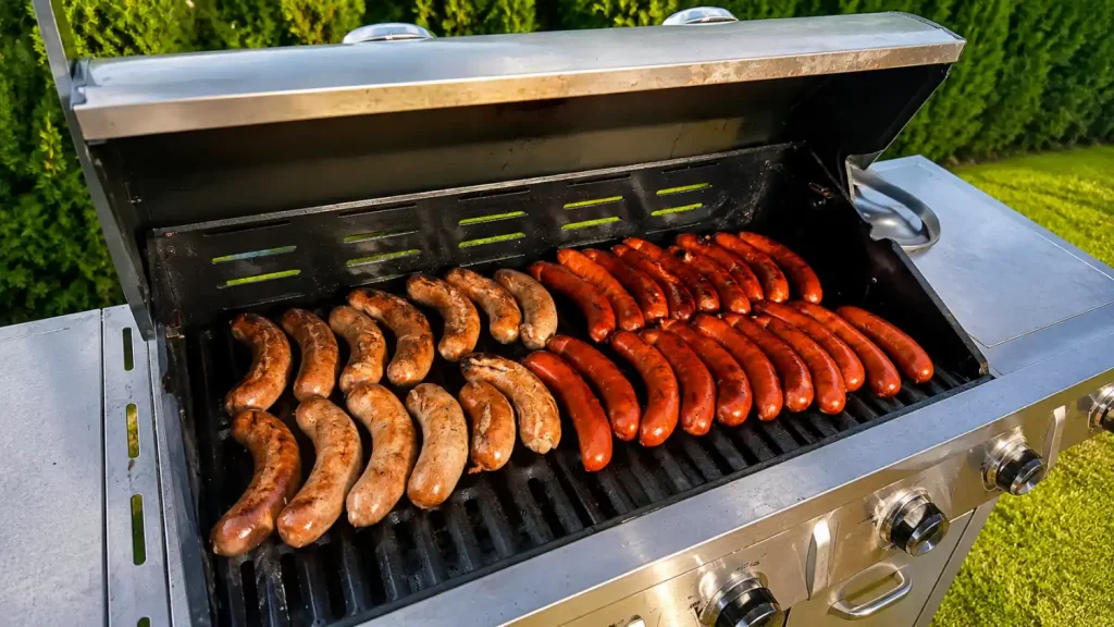 Ein Grill mit Würstchen und Steak im Freien auf einem Gartenplatz.
